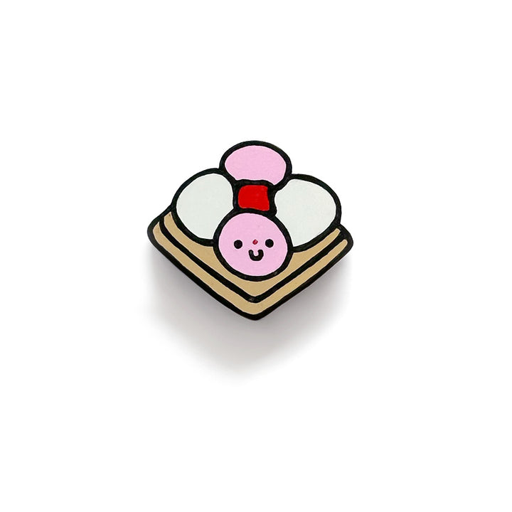 A cute art piece of a carita de bon bon, with pink and white balls on a tan square cookie and a smiley face on one of the balls, against a white background.