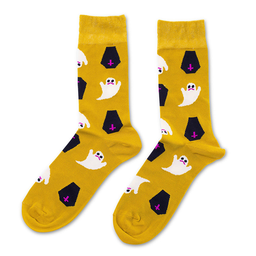 A pair of mustard yellow crew socks with a Halloween pattern featuring white ghosts and black coffin shapes with purple crosses, displayed against a solid white background.