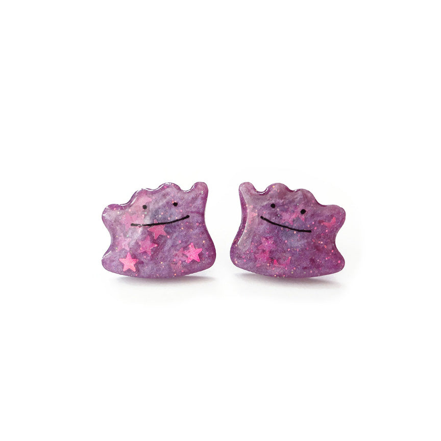 A pair of sparkly purple stud earrings in the shape of the Pokemon Ditto, a purple blob with a simple smiling face.