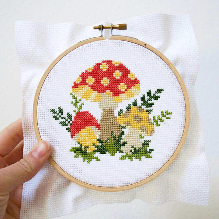 Hand holding a finished cross-stitch of a cluster of mushrooms.